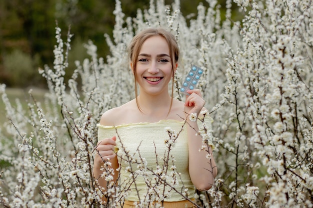 Frau mit Medizin in den Händen Fighting Spring Allergies Outdoor - Porträt einer allergischen Frau, umgeben von saisonalen Blumen.