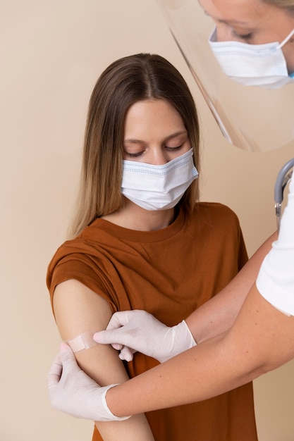 Frau mit medizinischer Maske, die nach einer Impfung einen Aufkleber am Arm bekommt