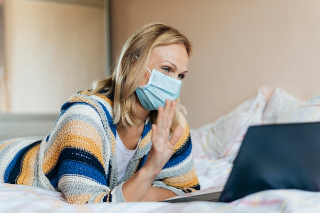 Frau mit medizinischer Maske in Quarantäne mit Laptop