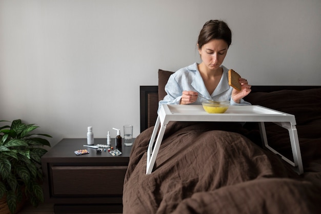 Frau mit mittlerer Aufnahme, die im Bett Suppe isst