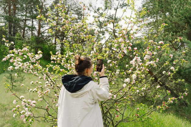 Foto frau mit mobiltelefon und fotografiert blühende frühlingsäpfelbäume.