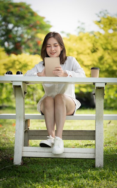 Frau mit nachdenklichem Lächeln im Park mit intelligenter digitaler Tablette Porträt eines jungen, charmanten Unternehmens