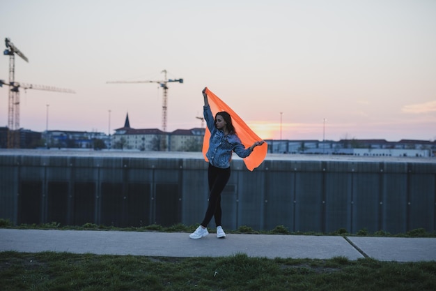 Foto frau mit orangefarbenem textilien steht bei sonnenuntergang gegen den himmel