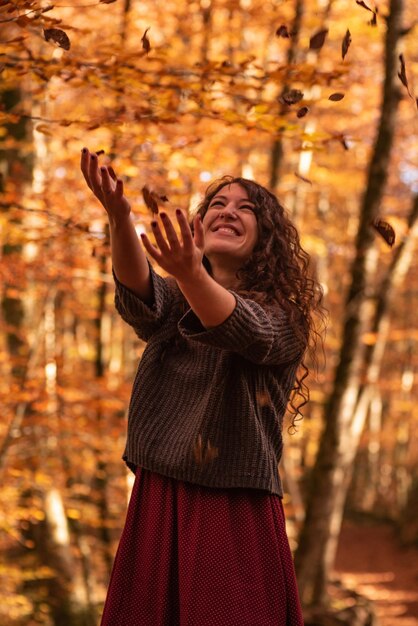 Frau mit orangefarbenen Blättern, die um Herbstbuchenwald fallen