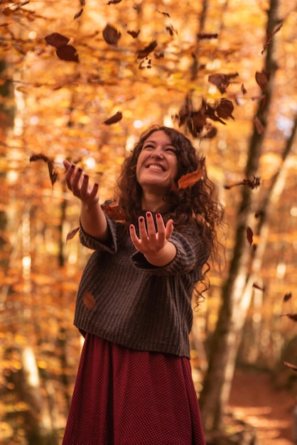 Frau mit orangefarbenen Blättern, die um Herbstbuchenwald fallen