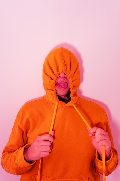 Foto frau mit orangefarbener kapuze steht gegen eine rosa wand