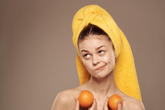 Frau mit Orangen in den Händen Emotionen nackte Schultern Handtuch auf dem Kopf beige Hintergrund Hochwertiges Foto