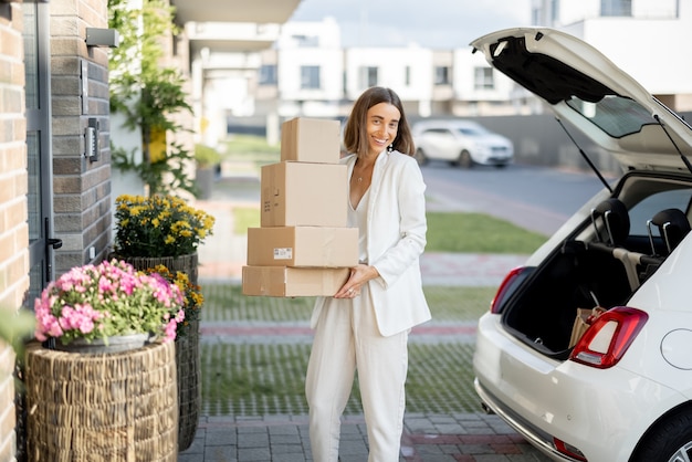 Frau mit Paketen in der Nähe ihres Autos und ihres Hauses