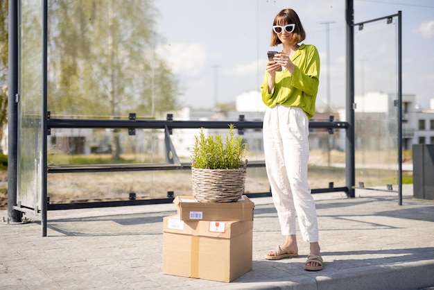 Frau mit Paketen und Blumentopf an einer Bushaltestelle