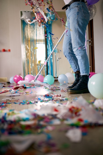 Frau mit pushbroom-reinigungsmüll vom boden im raum nach partykonfetti