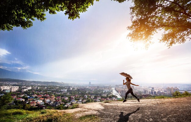 Frau mit Regenschirm, die bei Sonnenuntergang über das Stadtbild springt