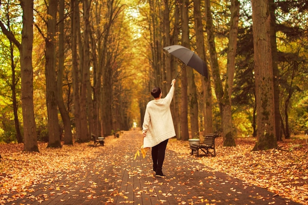 Frau mit Regenschirm geht im Herbstpark spazieren