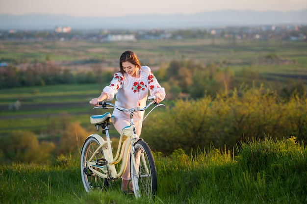 Frau mit Retro- Fahrrad auf dem Hügel am Abend