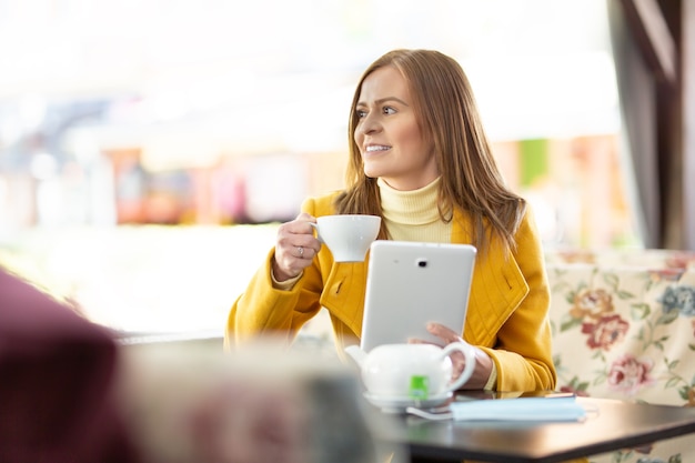 Frau mit Rollkragenpullover trinkt eine Tasse Tee mit einer Tablette in einem Café.