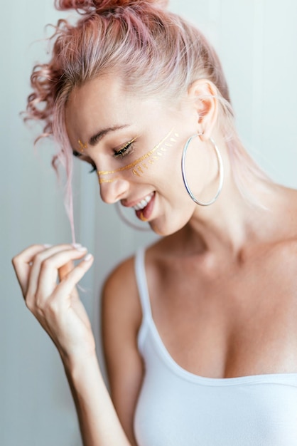 Frau mit rosa Haaren und künstlerischem Make-up in Form von Pinselstrichen, die beiseite schauen und auf hellweiß posieren