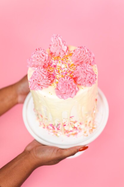 Frau mit rosa-weißer Buttercreme-Creme-Torte mit rosa Streuseln und weißem Schokoladen-Ganache-Tropf.