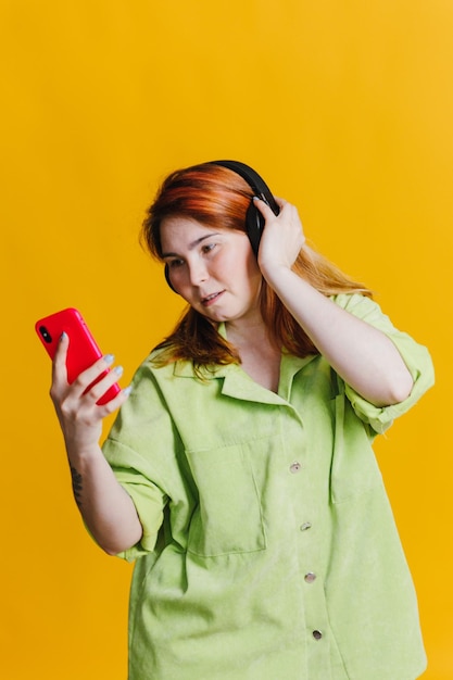 Frau mit roten Haaren, die über Kopfhörer Musik auf ihrem Telefon hört