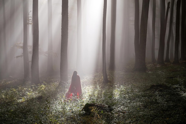 Frau mit roter Decke steht an Baumstämmen im Wald
