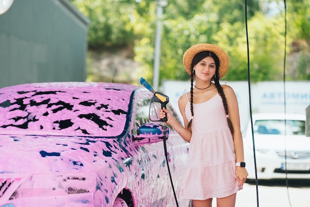 Frau mit Schlauch steht neben Auto, das mit rosa Schaum bedeckt ist