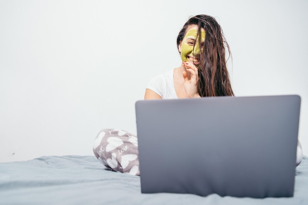 Frau mit Schönheitsmaske im Gesicht sitzt mit nassen Haaren auf dem Bett