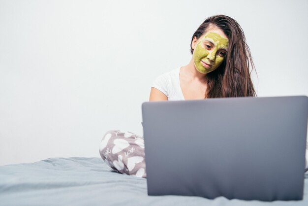 Frau mit Schönheitsmaske im Gesicht sitzt mit nassen Haaren auf dem Bett