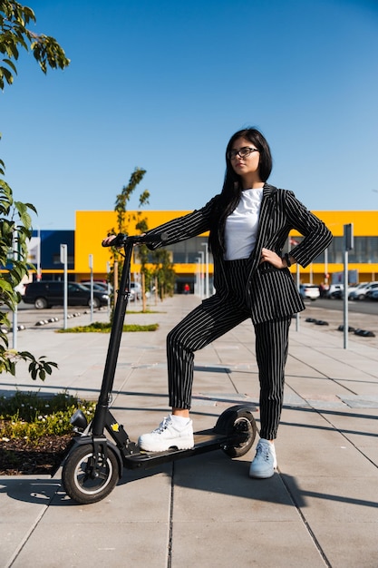 Frau mit Schubscooter steht auf dem Fußweg gegen den klaren blauen Himmel
