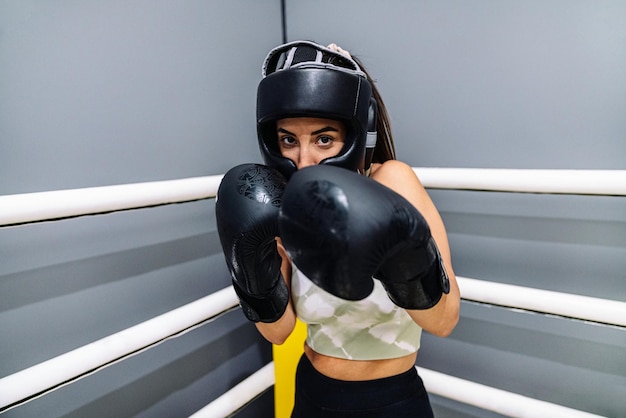 Frau mit Schutzhandschuhen und Kopfbedeckung in Angriffsposition auf einem Ringboxen