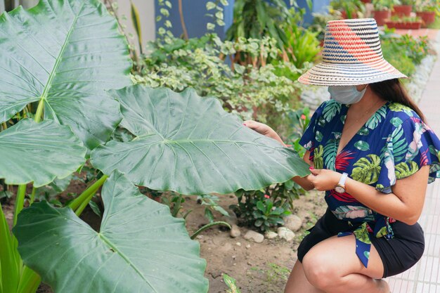 Frau mit Schutzmaske, die sich um Pflanzen in ihrem Garten kümmert. Großstadt-Dschungel.