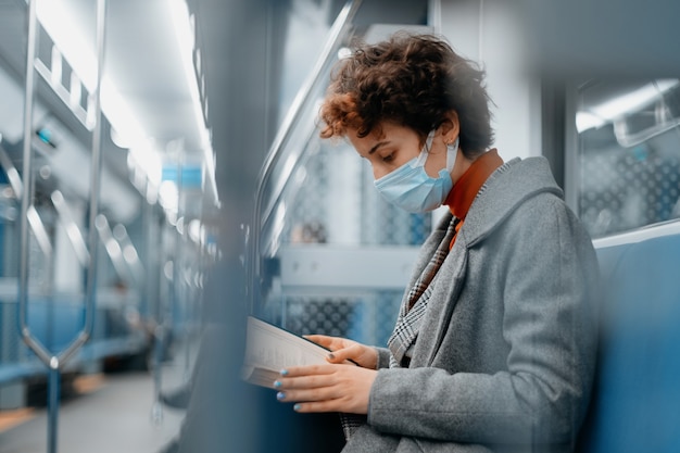 Frau mit Schutzmaske liest ein Buch in einer U-Bahn