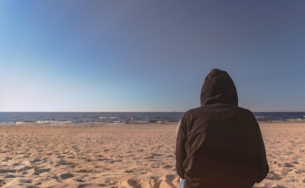 Frau mit schwarzem Hoodie am Strand Menschen sitzen im Sand und beobachten im