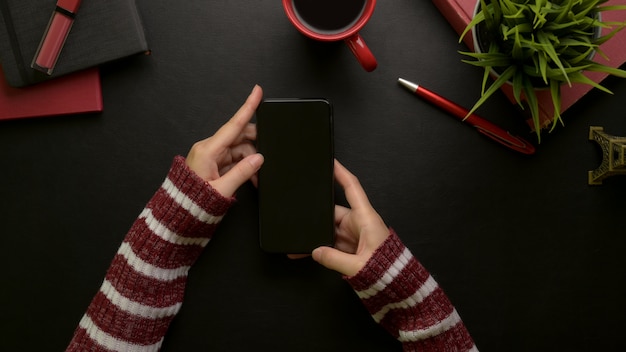 Frau mit Smartphone beim Sitzen am stilvollen Schreibtisch mit Kosmetik, Zubehör, Kaffeetasse und Dekoration