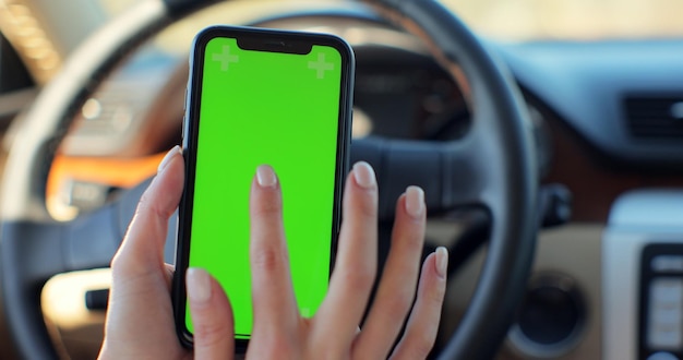 Frau mit Smartphone mit Greenscreen-Chroma-Schlüssel im Auto. Konzept: Fahrtrichtung, Adresssuche, Nachricht, Standort, Geschäft.