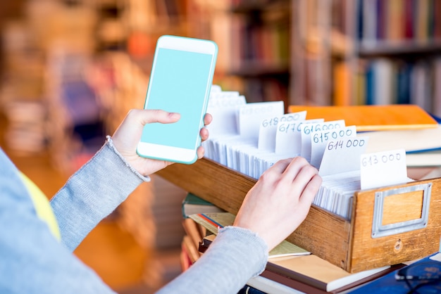 Frau mit Smartphone mit leerem Bildschirm in der Nähe des Kartenkatalogs in der Bibliothek