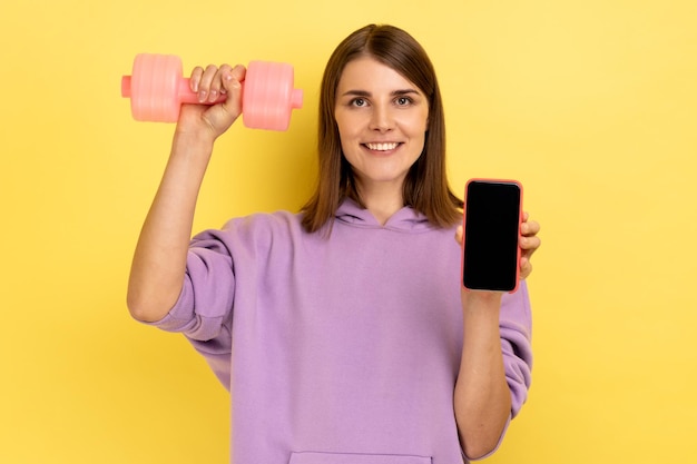 Frau mit Smartphone mit leerem Bildschirm und rosafarbener Hantel, die für neue Fitnessanwendung wirbt