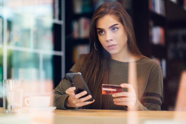 Frau mit Smartphone und Kreditkarte für Online-Shopping in einem Café