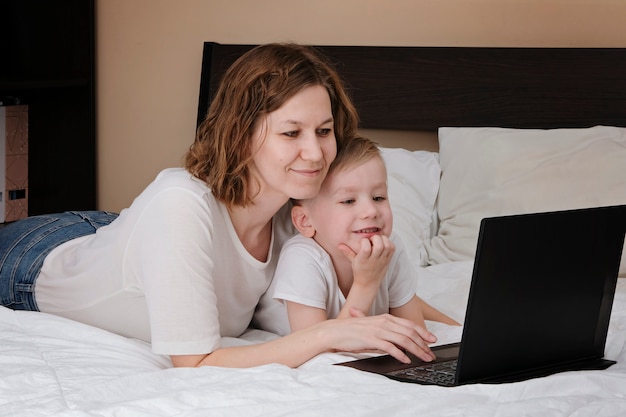 Frau mit Sohn, der auf dem Bett liegt, während Quarantäne des Koronavirus mit cpmputer.