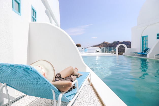 Frau mit Sommerhut, die sich auf einen entspannenden Stuhl zum Sonnenbaden am Pool legt