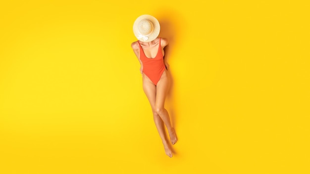 Foto frau mit sommerhut und orangefarbener badebekleidung entspannt gelben hintergrund