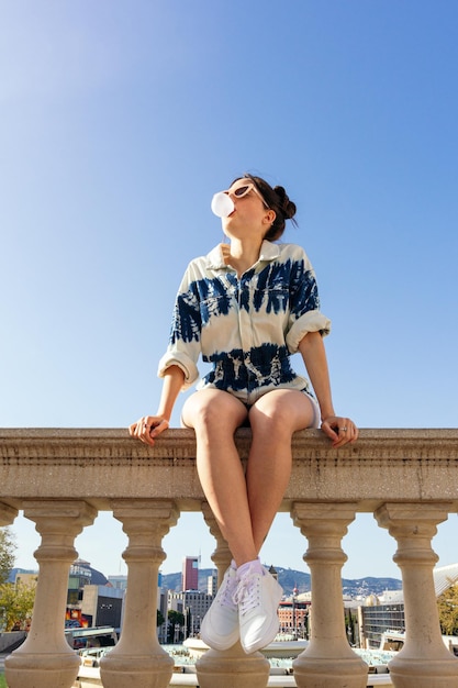 Frau mit Sonnenbrille, die eine Blase mit Kaugummi macht, die in der Stadt posiert