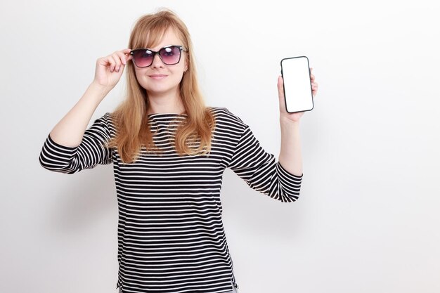 Frau mit Sonnenbrille mit Mockup-Smartphone auf weißem Hintergrund Sommerstimmung