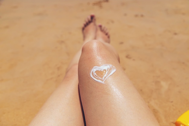 Frau mit Sonnencreme am Bein am Strand