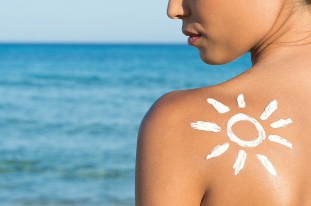 Frau mit Sonnencreme am Strand in Form der Sonne