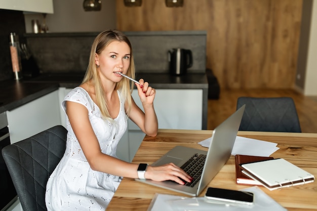 Frau mit Stift im Mund, der an Laptop-Computer zu Hause arbeitet