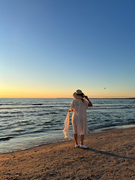 Frau mit Strw-Hut, die am Strand bei Sonnenuntergang am Meer spazieren geht