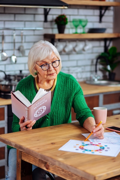 Frau mit stylischer grüner Strickjacke und Brille, die ein offenes Bibelbuch hält