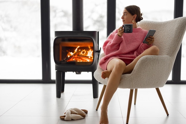 Frau mit Tasse auf Stuhl am Kamin im Haus auf Natur