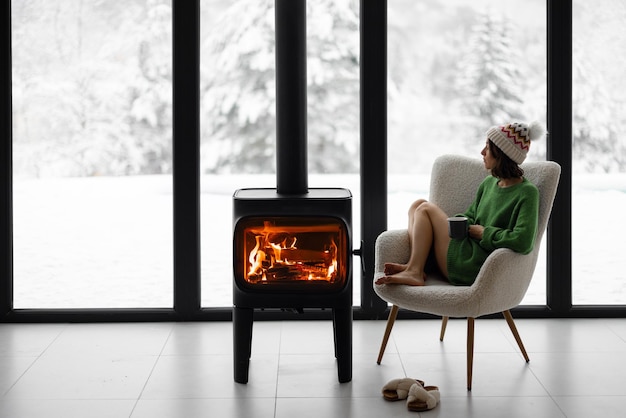 Frau mit Tasse auf Stuhl am Kamin im Haus auf Natur