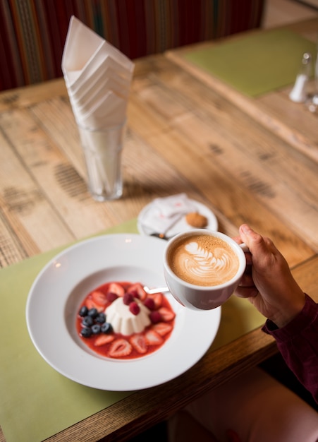 Frau mit Tasse Kaffee und weißem milchigem sahnigem Pudding mit Marmelade und Beeren