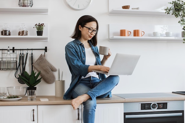 Frau mit Teetasse arbeitet von zu Hause aus mit einem Laptop