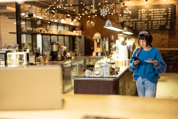 Frau mit Telefon, die ihre Bestellung im modernen Café trägt